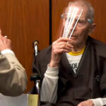 Robert Durst holds a face shield in front of him