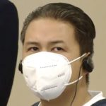 a man in a mask and wearing headphones looks at the camera in court