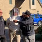 Rorie S. Woods, 55, of Hadley, Mass., center, wears a beekeeping suit while taken into custody by Hampden County Sheriff's Department officers, in Longmeadow, Mass., Wednesday, Oct. 12, 2022.