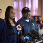 People speak at a press conference with a photo of a football player behind them