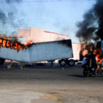 Men ride on a motorcycle past a burning truck on the streets of Culiacan