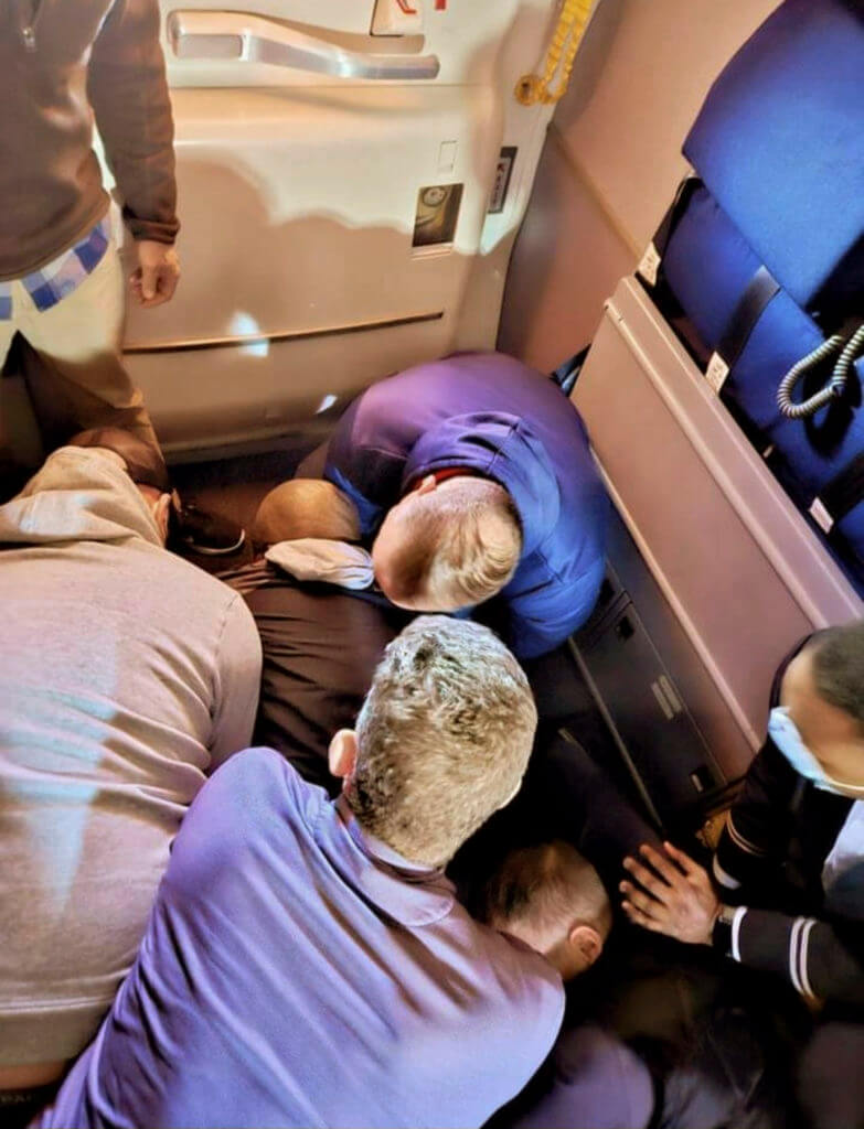 Passengers and crew restrain a man who tried to open a plane's emergency door and tried to stab a flight attendant.