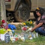 A woman places flowers at a memorial.