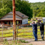 Two people stand at a fence with a building in the background