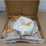 Open pizza box with paper plate, crumpled aluminum foil and pizza crusts.