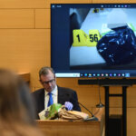 Man sits on witness stand with images of evidence on monitor behind him