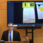 man sits on witness stand with evidence photos behind him