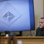 A man testifies in front of a photo of a ceiling vent