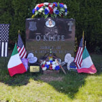 Flags, flowers and remembrances flank the headstone