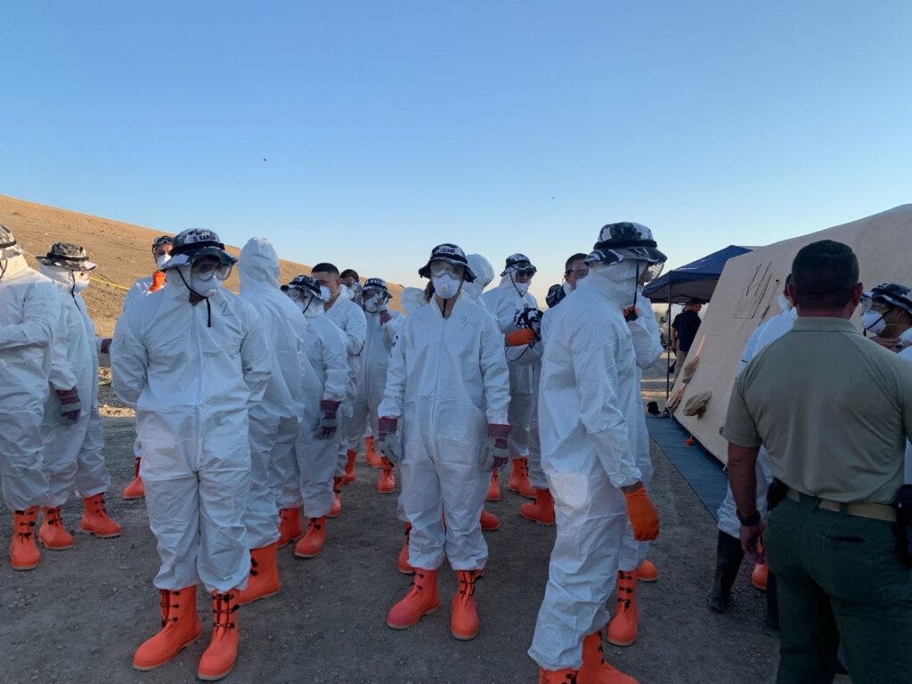 people in masks, white suits and orange boots in a line