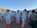 people in masks, white suits and orange boots in a line