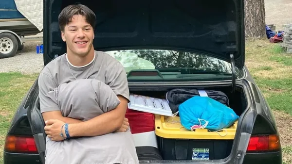 Josiah Kilman stands with a pillow outside a car