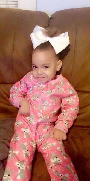 A'Niyah Perry sits on a couch in PJs with a bow in her hair